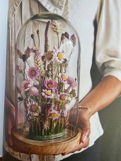 a woman holding a glass dome with flowers in it