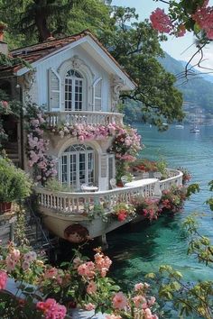 a house on the water with flowers growing out of it's windows and balconies