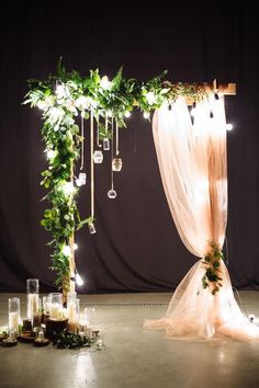 a wedding arch decorated with greenery and hanging ornaments is lit up by candles on the floor