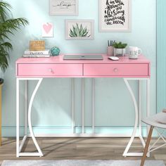 a pink desk sitting in front of a blue wall with pictures on the wall above it