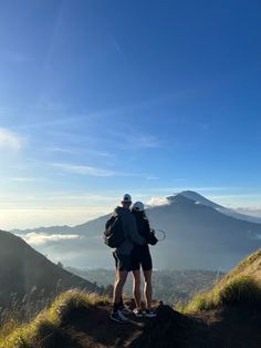 two people standing on top of a mountain with their backs to each other looking at the view