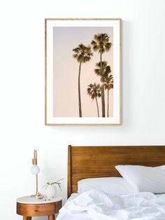 a bed with white sheets and two palm trees on the wall above it in a bedroom