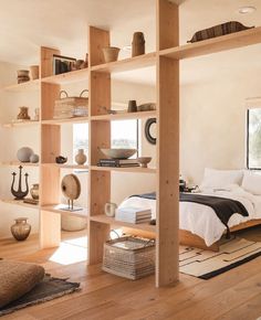 a bed sitting in a bedroom next to a wooden shelf filled with books and bowls