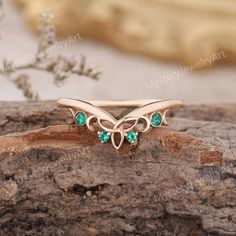 a gold ring with green stones on top of a tree branch in front of a rock