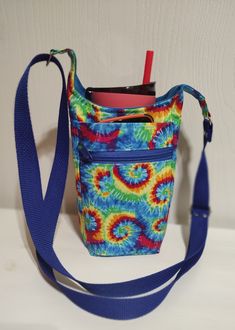 a multicolored tie - dyed bag with a blue strap and a straw in it