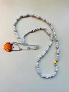 a white beaded necklace with an orange and yellow object on it's end