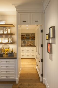 an open kitchen with white cabinets and wood flooring in the hallway leading to another room