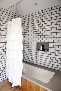 a white shower curtain in a bathroom next to a bathtub and wooden flooring