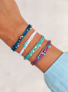 a woman's arm with four different bracelets on top of her wrist and one is wearing a blue shirt