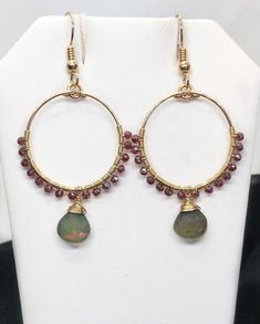 Ethiopian Opal and Garnet when paired with 14k Gold Filled components result in a elegant pair of earrings! ❤️ MATERIALS USED      ▪️Ethiopian Opals: These smooth, opaque stone flash shades of red, orange            and green. The stones measure 8mm (w) x 8mm (h).      ▪️Garnet: These dark red, round, faceted stones measure 2mm.      ▪️14k Gold Filled: The wire and ear wire are Gold Filled. ❤️ MEASUREMENTS       ▪️The hand shaped hoop measures 7/8" in diameter. With the garnet stones,            the hoop measures 1-1/16" diameter. ❤️ LENGTH      ▪️ The earring hangs 1-7/16" from the bottom of the ear wire and 2-1/4" from the             top of the ear wire. ❤️ PROCESSING TIME      ▪️The item will be processed and shipped within 1-3 business days from the                   time the order is Elegant Christmas Drop Earrings, Elegant Round Christmas Earrings, Elegant Christmas Jewelry With Dangle Shape, Gemstone Dangle Jewelry For Celebrations, Dangle Gemstone Jewelry For Celebration, Celebration Dangle Gemstone Jewelry, Celebration Dangle Jewelry With Gemstones, Christmas Celebration Jewelry With Matching Earrings, Handmade Briolette Earrings For Anniversary