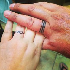 two people holding hands with tattoos on their fingers and the other hand has a ring