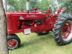 an old red farmall tractor parked next to a tree