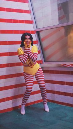 a woman dressed as a clown posing in front of a red and white striped wall