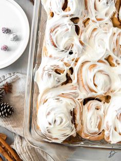 a pan filled with cinnamon rolls covered in icing next to other baking supplies and christmas decorations