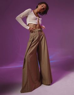 a woman standing in front of a purple background wearing wide legged pants and a crop top