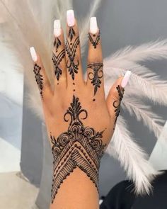 a woman's hand with henna tattoos on it and feathers in the background