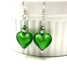 Handmade small green heart earrings featuring emerald green, Venetian Murano heart shaped beads; sterling silver; and  crystals. These beautiful earrings are composed of 14mm heart shaped Venetian Murano glass beads crafted by Italian glass artists . The beads have a core of white gold foil encased within emerald green glass.  crystals add sparkle. Sterling silver beads, head pins and earring wires complete these lovely earrings. These earrings are 1.5 inches (3.8cm) long measured from the top a Glass Bead Crafts, Murano Glass Earrings, Earrings Emerald, Valentines Earrings, Earring Wire, Earring Wires, Green Heart, Murano Glass Beads, Head Pins