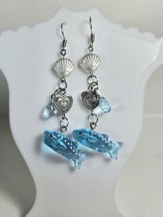 two blue glass dolphins with seashells hanging from them'dangles on a white plate