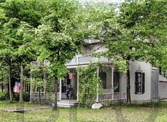 an old house with ivy growing on it's sides and trees surrounding the porch