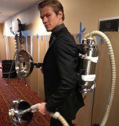 a man in a suit and tie is holding a large metal object with two hoses attached to it