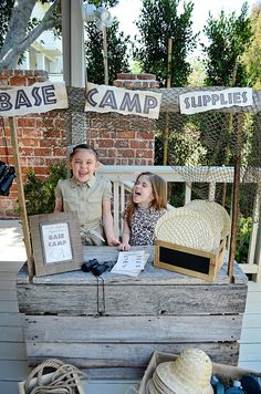 two children are sitting on a bench with hats and other items around them in front of a sign that says camp supplies