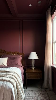 a bed sitting next to a window with a lamp on top of it in a bedroom