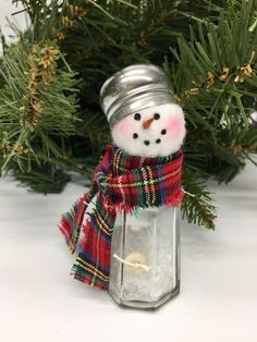 a small snowman in a plaid scarf and hat is sitting inside a glass jar