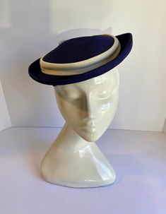 Vintage 1950's Ladies navy Blue Hat. Size small. Cream colored trim and back bow. Good condition. Content: Linen or straw?  Dimensions: Overall width with brim 9"W x 9-1/2"D x 2"H overall with clips. Clip height 1-3/4"H. Inside width 6-1/2"W. No label. Some crushing on top. See photos. No rips, tears, or stains. Fitted Navy Wide Brim Hat, Vintage Blue Hat With Curved Brim, Navy Fitted Wide Brim Hat, Vintage Blue Adjustable Hat Bands, Navy Fitted Hat With Short Brim, Vintage Blue Short Brim Hat, Vintage Navy Hat With Curved Brim, Blue Fitted Wide Brim Cloche Hat, Blue Wide Brim Cloche Hat