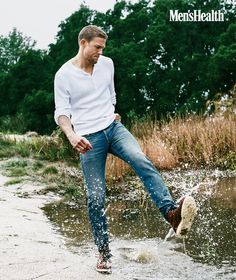 a man in white shirt and jeans kicking up water with his foot on the ground