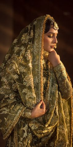 a woman dressed in green and gold is posing with her hands on her chin, looking to the side