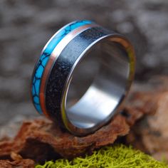 a wedding ring with blue and black inlays on top of moss covered rocks