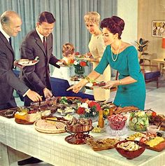 a group of people standing around a table filled with food