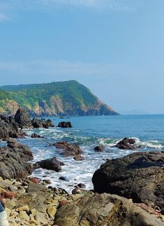 a person standing on rocks near the ocean with an island in the distance behind them