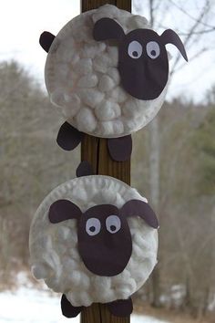 two sheep are hanging from a wooden pole in the snow with eyes drawn on them