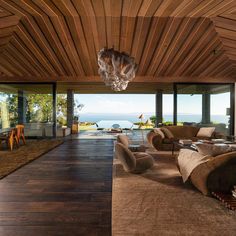 a living room with wooden ceilings and floor to ceiling windows overlooking the ocean is shown