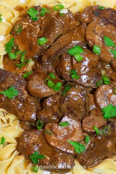 a white plate topped with pasta and meat covered in gravy next to green garnish