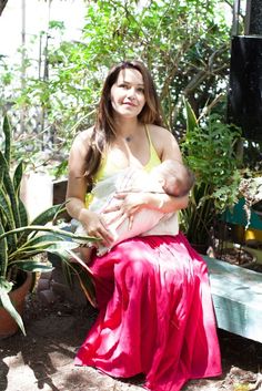 a woman holding a baby in her arms while sitting on a bench next to plants