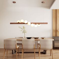 a dining room table and chairs with lights hanging from the ceiling above it, in front of a white wall