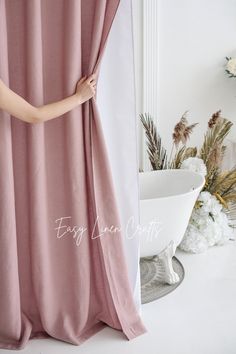 a woman is opening the curtain to reveal her pink dress in front of a white bathtub