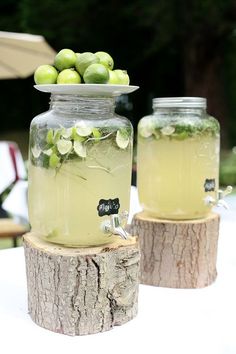 two mason jars filled with lemonade and limes sitting on top of a tree stump