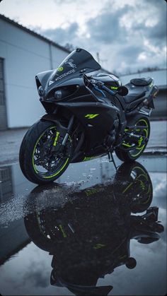 a black motorcycle parked in front of a building on a wet surface with its reflection