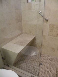 a walk in shower sitting next to a glass door with a bench on the side