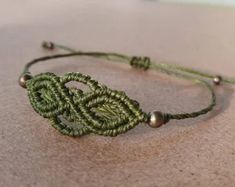 a close up of a green string bracelet on a table with beads and an object in the background