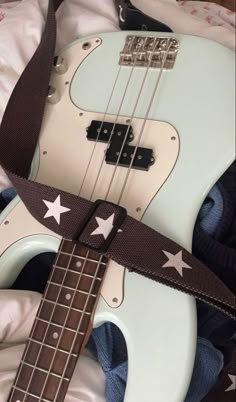 a white guitar with stars on it and a brown strap around the neck is laying on a bed