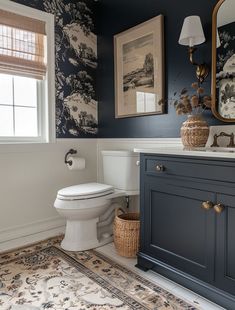 a white toilet sitting in a bathroom next to a blue vanity and window with pictures on it