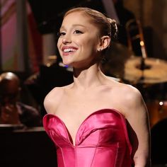 a woman in a pink dress standing next to a drum set and smiling at the camera