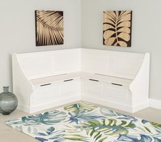 a white corner bench sitting on top of a rug next to a vase and two paintings