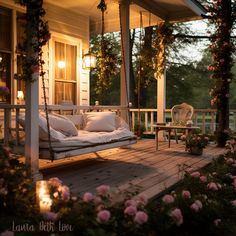 a porch swing with pillows on it and flowers in the foreground, lit by lanterns