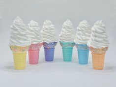 six ice cream cones with white frosting and sprinkles are lined up