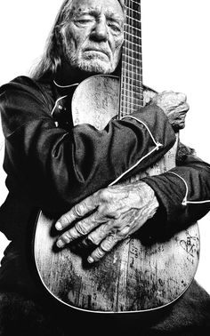 an old man is holding a guitar in his hands and looking at the camera with one hand